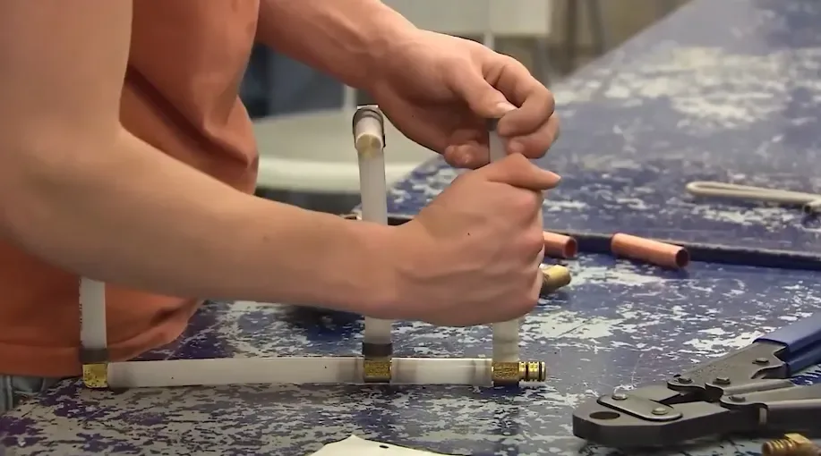 Plumber crimping fittings on new water supply pipe at a workbench