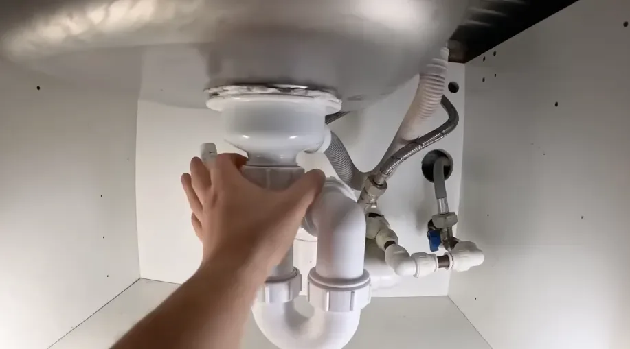 Hand adjusting the P-trap and drain under a kitchen sink