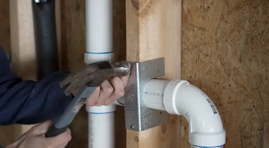 Plumber tightening a PVC drain fitting inside an open bathroom wall