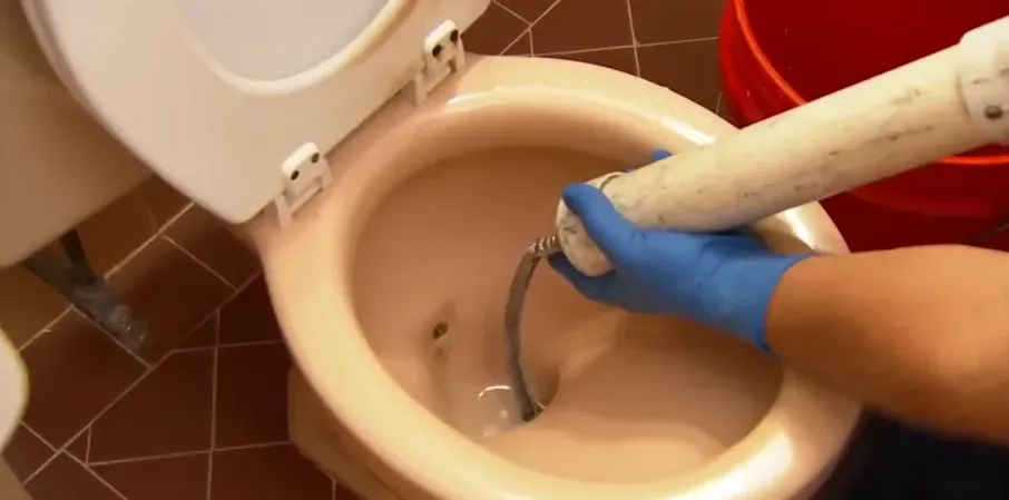 Plumber using a closet auger to clear a clogged toilet
